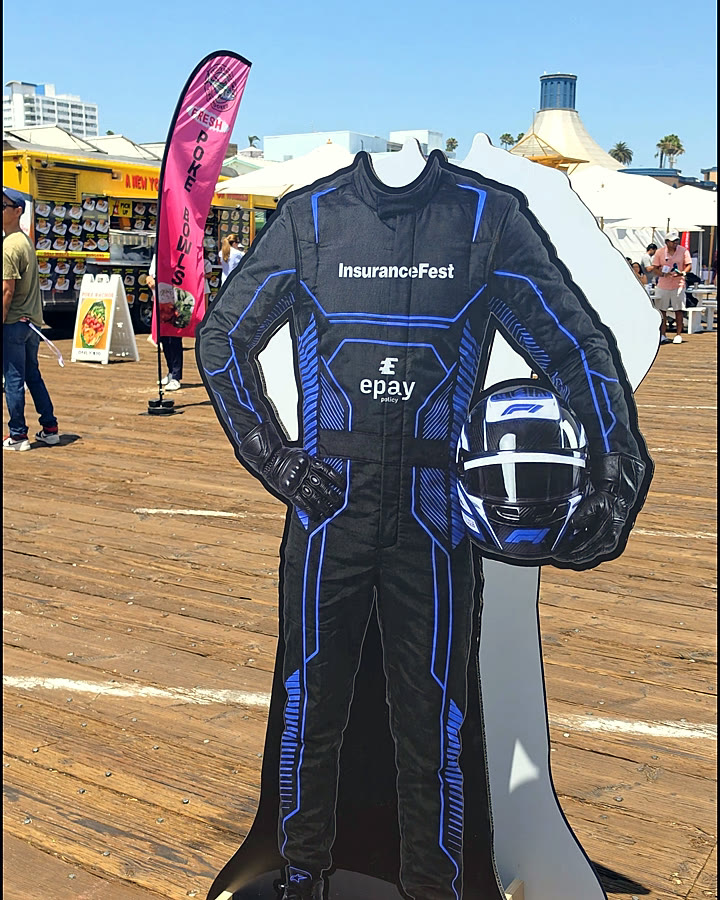 Formula-driver cut-out in an Epay Policy racing suit on the pier deck at Insurance Fest