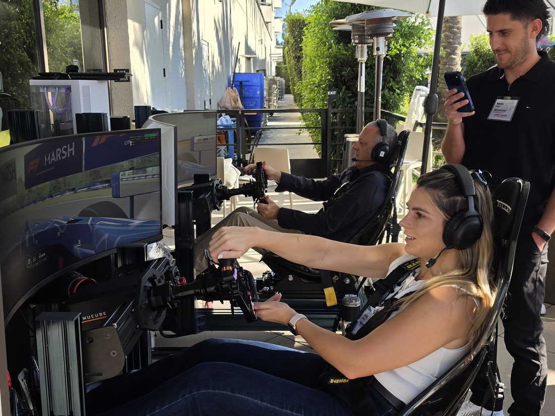 A Trackside attendant on the floor beside a guest driving a full-motion racing simulator